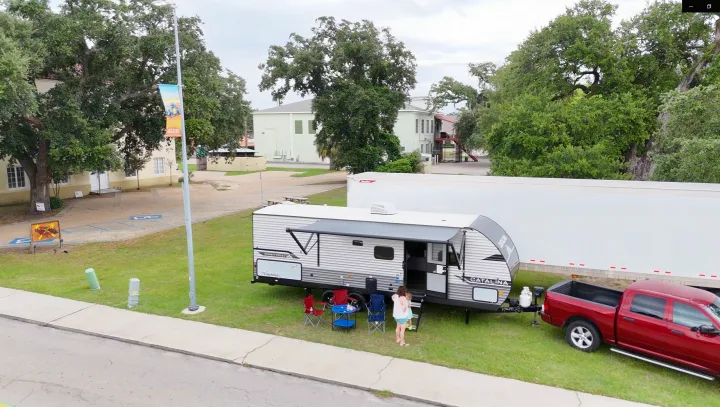 An RV rental is set up for camping on grass, with a red truck, chairs, and a family preparing for outdoor fun.. Coachmen Catalina 2024