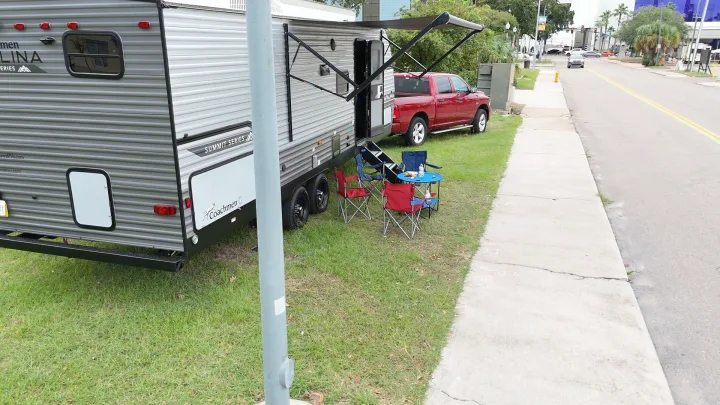 An RV rental, a grey travel trailer, is parked on grass with an extended awning, red truck, and outdoor seating.. Coachmen Catalina 2024