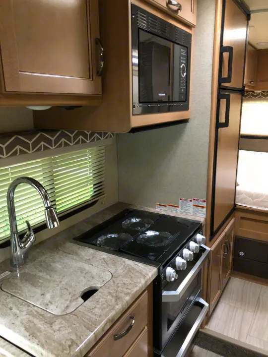Modern RV rental kitchen with sink, stove, microwave, fridge, and ample storage for comfortable travel.. Thor Daybreak 2020