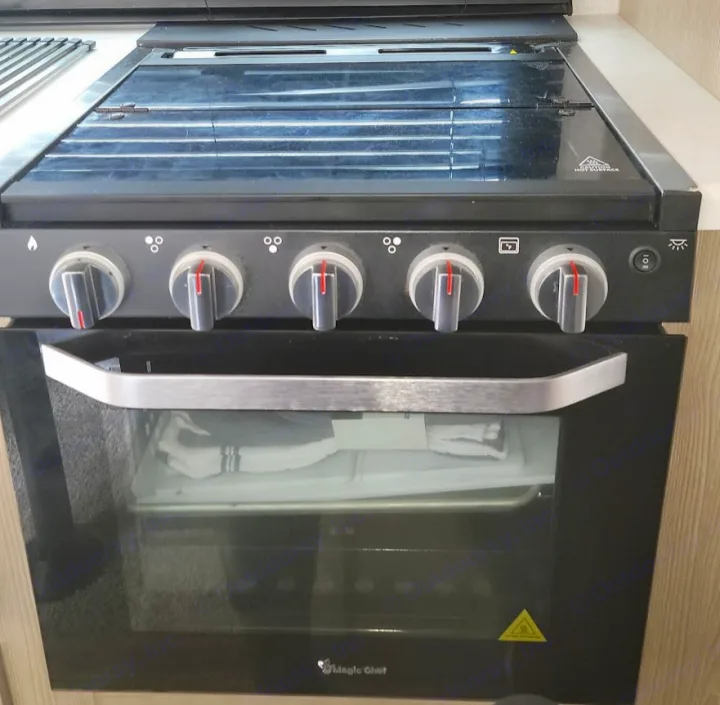RV rental kitchen: Black Magic Chef gas stove/oven with a glass cooktop cover and five control knobs.. Forest River Rockwood Geo Pro 2022