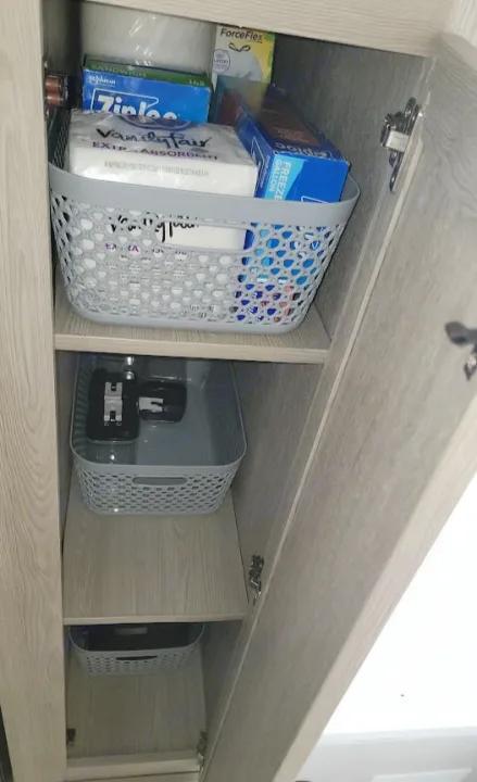 RV rental cabinet with organized shelves of household supplies: paper towels, Ziploc bags, and other items in grey baskets.. Forest River Rockwood Geo Pro 2022