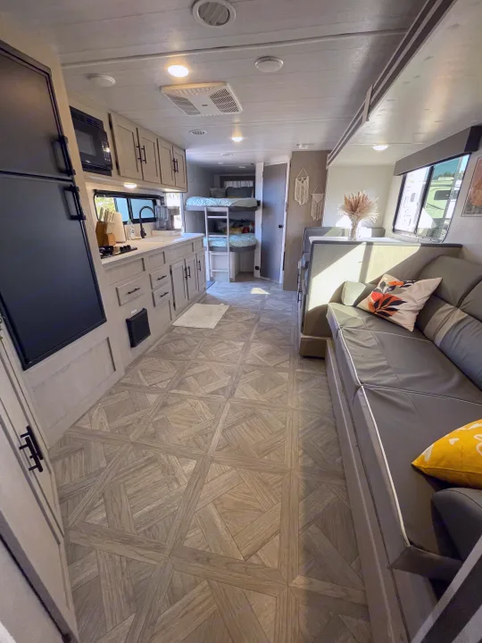 Spacious RV rental interior features a kitchen, living area with sofa, and bunk beds at the rear of the vehicle.. Forest River Wildwood X-Lite 2024