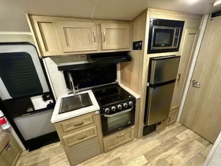 Modern rv rental kitchen with stainless steel fridge, microwave, stove, oven, and sink. Compact and fully equipped for travel.. Forest River Rockwood Geo Pro 2022
