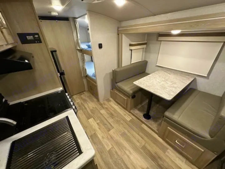 RV rental interior: kitchen with stove & sink on left, dining booth with table on right, and bunk beds in back.. Forest River Rockwood Geo Pro 2022