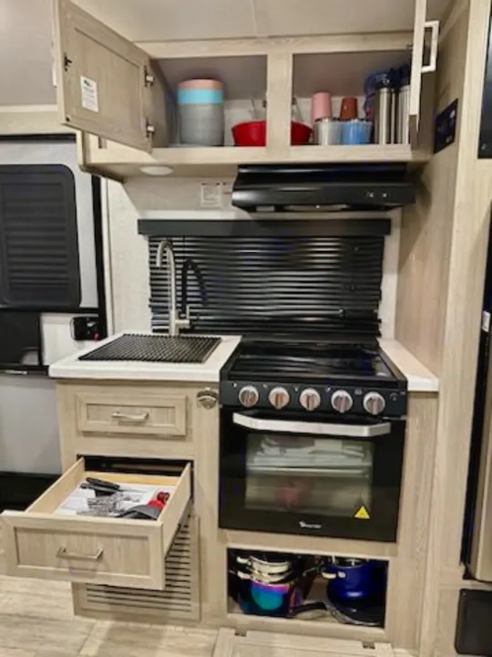 Compact RV rental kitchen showcasing sink, stove, oven, cabinets, and utensil drawer for convenient camping trips.. Forest River Rockwood Geo Pro 2022