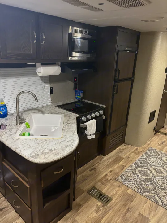 RV rental kitchen showing a well-equipped space with a sink, stove, microwave, and refrigerator, all in a stylish, compact design.. Keystone RV Summerland 2018