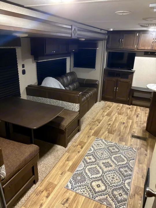 This clean RV rental features a cozy brown sofa, dinette, and entertainment center with wood-look flooring.. Keystone RV Summerland 2018