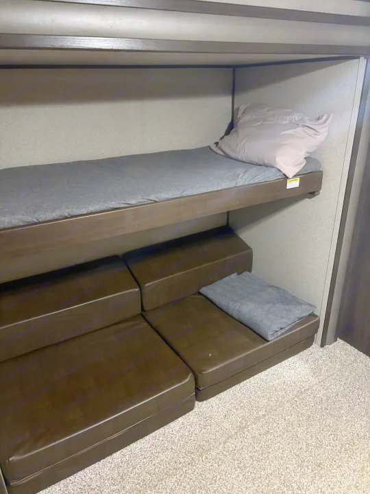Comfortable RV rental bunk bed with grey mattress, plus versatile brown seating/sleeping cushions below.. Keystone RV Summerland 2018
