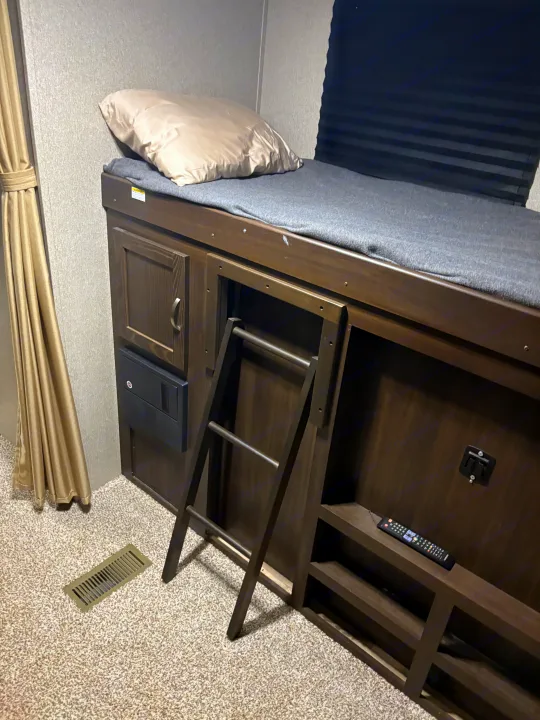 RV rental sleeping area: a bunk bed with a pillow, gray blanket, ladder, and built-in storage. Ideal for travel.. Keystone RV Summerland 2018