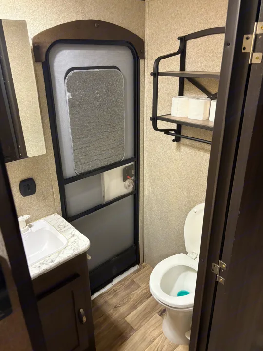 Inside an RV rental: compact bathroom with sink, toilet, shelving, and a typical RV entry door.. Keystone RV Summerland 2018