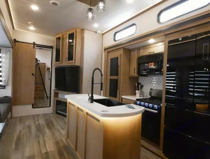 Spacious and modern RV rental interior features a well-equipped kitchen island, living area, and wood-look floors.. Forest River Sabre 2023