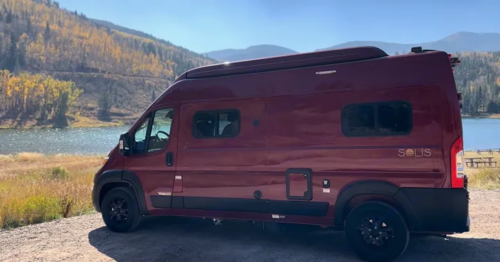 Maroon Winnebago Solis campervan by a fall lake. Explore nature with an RV rental.. Winnebago Solis 2023