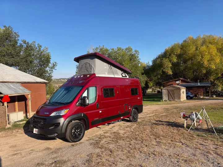 Red Winnebago Solis camper van with pop-top extended, parked in a rural setting, perfect for your RV rental.. Winnebago Solis 2023