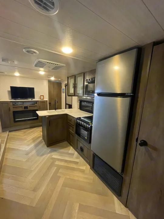 Modern RV rental interior featuring a well-equipped kitchen, living area with TV, and herringbone flooring.. Forest River Salem Cruise Lite 2022