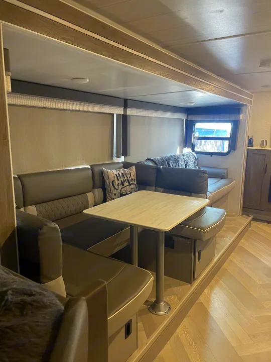 RV rental dinette: U-shaped seating, table, and modern light wood interior. Includes 'Happy Camper' pillow.. Forest River Salem Cruise Lite 2022