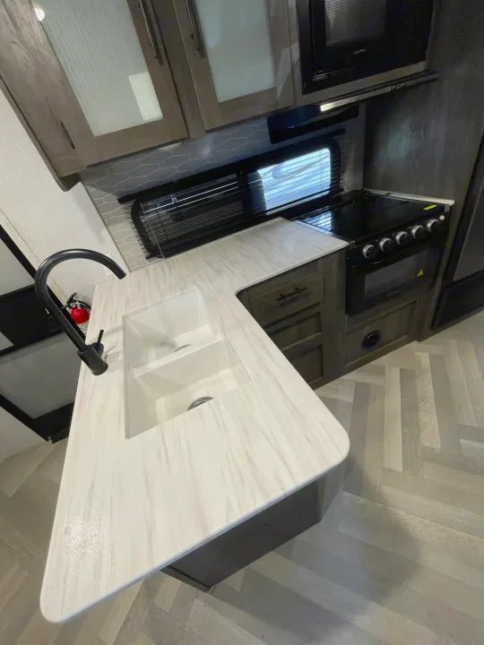 Modern RV rental kitchen featuring light countertops, double sink, black stove, microwave, and herringbone flooring.. Forest River Salem Cruise Lite 2022