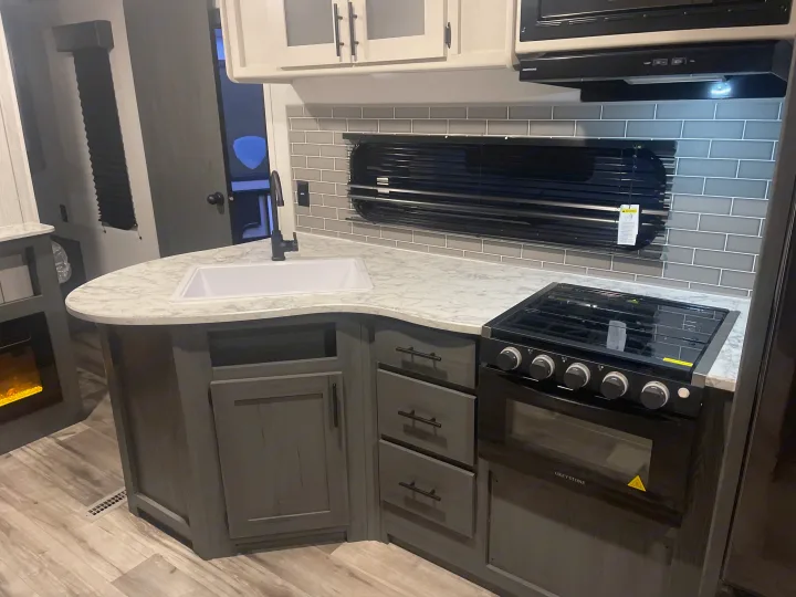 Modern RV rental kitchen featuring a white marble-look counter, sink, stove, grey cabinets, and subway tile backsplash.. Dutchmen 26bhc 2024