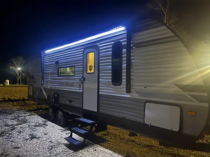 Brightly lit RV rental travel trailer parked on gravel at night, inviting you to your next outdoor camping adventure.. Dutchmen 26bhc 2024