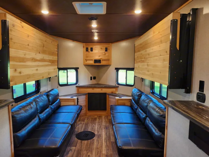 Spacious RV rental interior featuring comfortable seating, wooden walls, and an ice fishing hole on the floor.. Glacier Ice House 17RBLE 2023