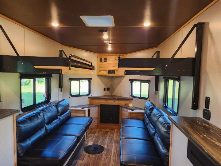 Inside a modern **rv rental**: black leather sofas, overhead bunk beds, and wood-toned finishes create a cozy, functional living space.. Glacier Ice House 17RBLE 2023