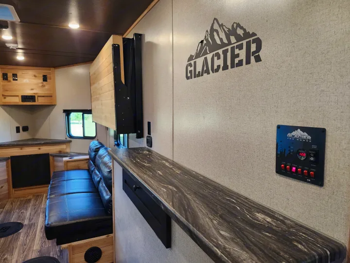 Step inside this Glacier Ice House RV rental, featuring a cozy sofa, wooden interior, and full control panel. Your adventure awaits!. Glacier Ice House 17RBLE 2023