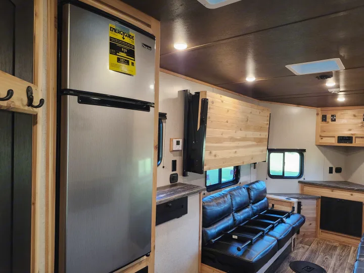 This RV rental interior showcases a stainless steel Magic Chef refrigerator, a cozy sofa, and a fold-up wooden bed/bench.. Glacier Ice House 17RBLE 2023