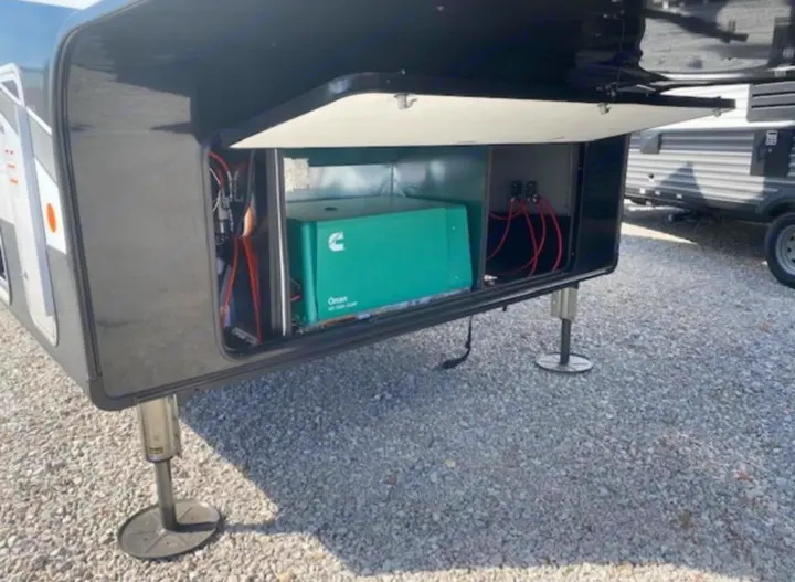 Front compartment of an RV rental revealing a green Cummins Onan generator, providing power for your adventures.. Jayco Seismic 2023