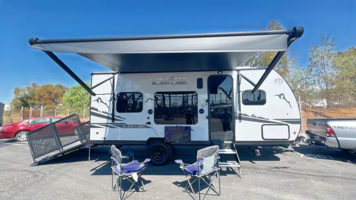 This white Cherokee Black Label travel trailer, perfect for an RV rental, is set up for outdoor fun with an extended awning & chairs.. Forest River Wolf Pup 2025