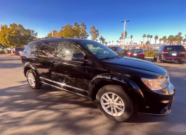 A shiny black SUV is parked in a sunny lot with palm trees. This vehicle offers a great ride; compare it with an rv rental for trips.. Dodge Journey 2016