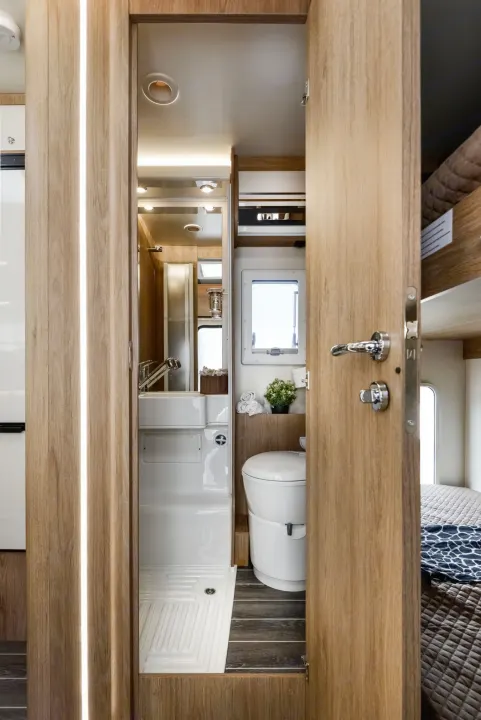 Modern RV rental interior: a compact bathroom with shower, toilet, and sink, beside a bunk bed.. Roller Team 707 Auto Roller 2025