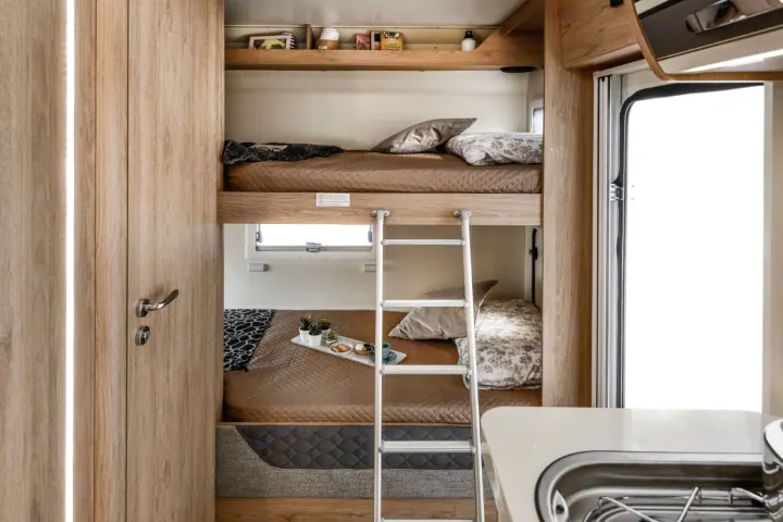 Interior of an RV rental features cozy bunk beds with quilted bedding, a ladder, window, and a snack tray. Compact travel comfort.. Roller Team 707 Auto Roller 2025