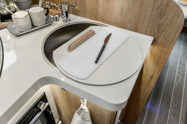 This compact RV rental kitchen boasts a sink with a cutting board cover, faucet, mugs, and an oven below the counter.. Roller Team 707 Auto Roller 2025