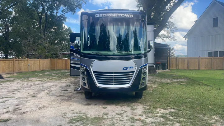A modern Georgetown GT7 RV rental parked outdoors, showing its front. Trees and a wooden fence provide a natural backdrop.. Georgetown GT7 2022