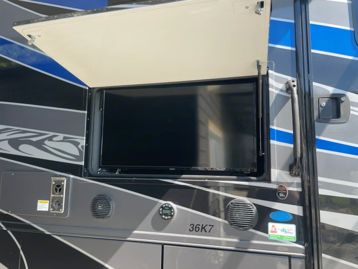 An RV rental showing its outdoor TV compartment with a lifted cover, speakers, and audio controls for entertainment.. Georgetown GT7 2022