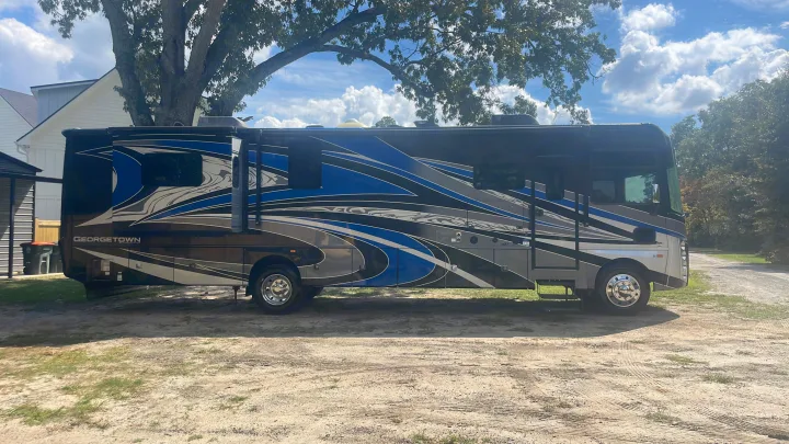 Large Class A motorhome, great for an RV rental, with blue/grey graphics, parked outdoors under a tree.. Georgetown GT7 2022