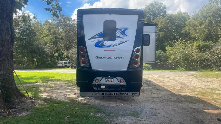 Rear view of a Georgetown motorhome, potentially an RV rental, with a slide-out extended in a wooded campsite.. Georgetown GT7 2022