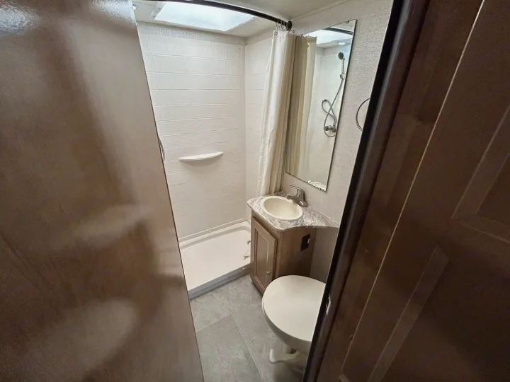 Explore a clean, compact RV rental bathroom: shower, sink, toilet, and vanity – perfect for your road trips.. Coachmen Leprechaun 2020