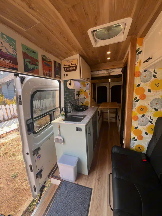 Step into this modern RV rental's camper van interior, featuring a functional kitchen, cozy living space, and wood-paneled ceiling.. Ford Transit 2023