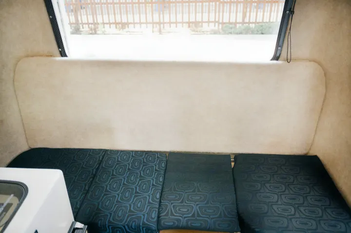 Cozy RV rental interior: cream-colored walls, dark patterned bed cushions, and a bright window overlooking a fence.. Outback Trailer Manufacturing the Outback 2017