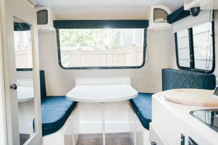 Explore this cozy RV rental interior! Features a dinette with blue cushions, large windows, and compact kitchenette.. Outback Trailer Manufacturing the Outback 2017