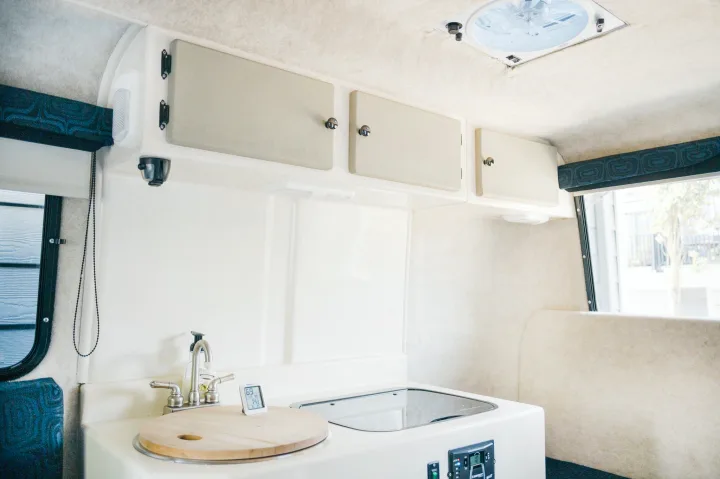 Inside a modern RV rental: a compact kitchen with sink, covered stove, white cabinets, and ceiling vent.. Outback Trailer Manufacturing the Outback 2017