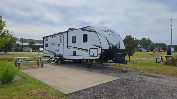 A white Sunset Trail RV rental is parked on a concrete pad at a campground site with a picnic table.. Crossroads Sunset Trail Super Lite 2022
