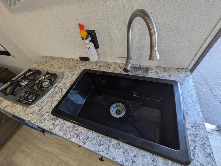 RV rental kitchen with a sleek black sink, two-burner stove, flexible faucet, and a unique flame nightlight.. Sunset Park & Rv Inc. 19rb 2025