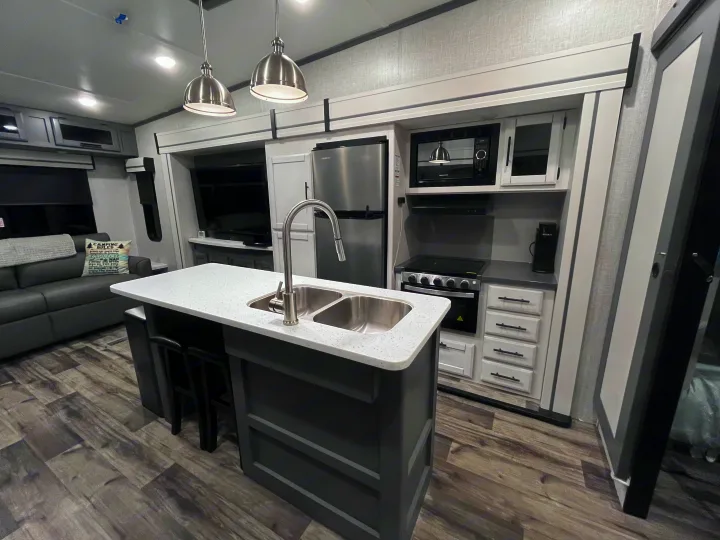 Modern RV rental interior with full kitchen, island, and cozy living area featuring a sofa and TV.. Volante 375MD 2023