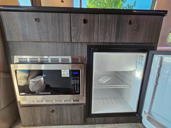 Compact kitchen in an RV rental, showing a Contoure microwave and a Vitrifrigo refrigerator with its door open.. Grech Strada Ion 2022