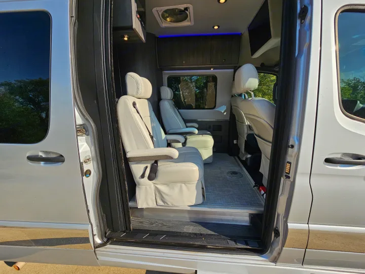 View into a modern RV rental through its open side door, showcasing light captain seats, overhead storage, and blue accent lighting.. Grech Strada Ion 2022