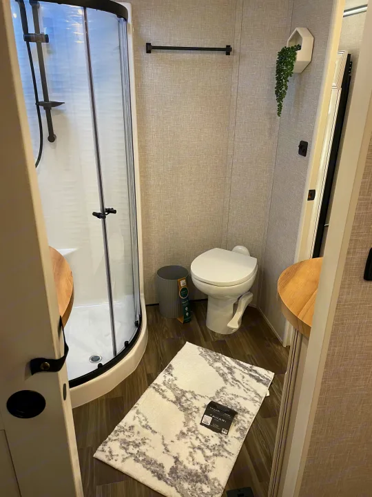 Bright, compact RV rental bathroom with a curved shower, toilet, and contemporary wall decor, perfect for travel.. Highland Ridge RV Open Range 2024