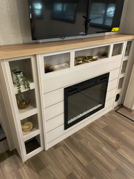 This RV rental's living space features a TV above a decorative console with open shelving, an electric fireplace, and modern decor.. Highland Ridge RV Open Range 2024