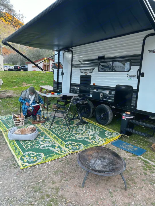 Cozy RV rental campsite. A person in a robe reads, dog rests, fire pit ready for ambiance.. Forest River Wildwood X-Lite 2022