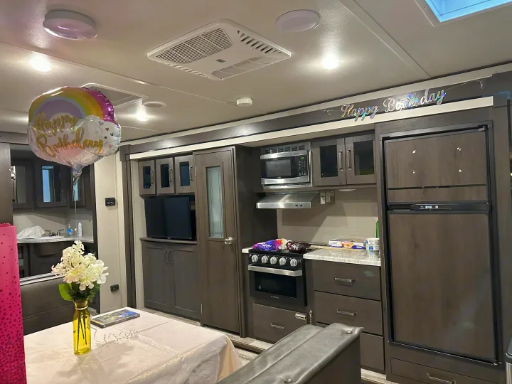 Cozy RV rental interior decorated for a birthday, featuring a compact kitchen, living space, and modern appliances.. Grand Design Transcend Xplor 2021